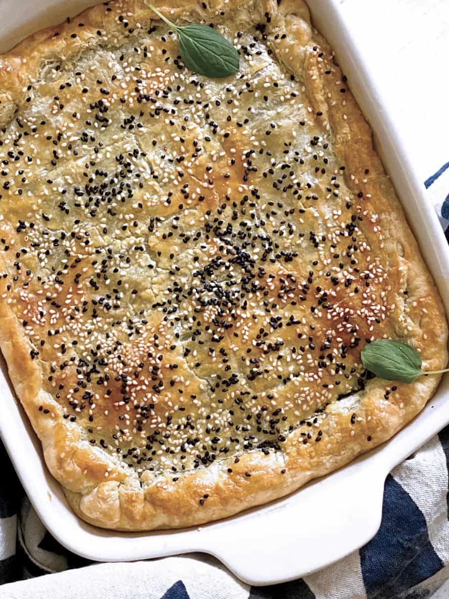 Savory pie crust with sesame seeds in a white baking pan and a cloth napkin.