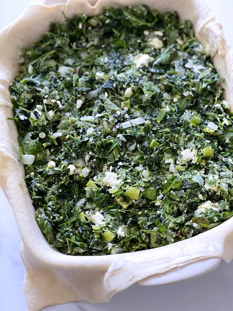 Diced onion, spinach and scallions over puff pastry in white baking pan.