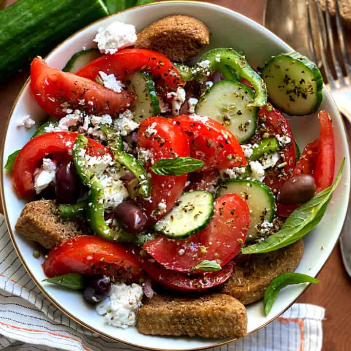 A salad in a white plate with a serving spoon an olive oil bottle and fresh basil leaves.
