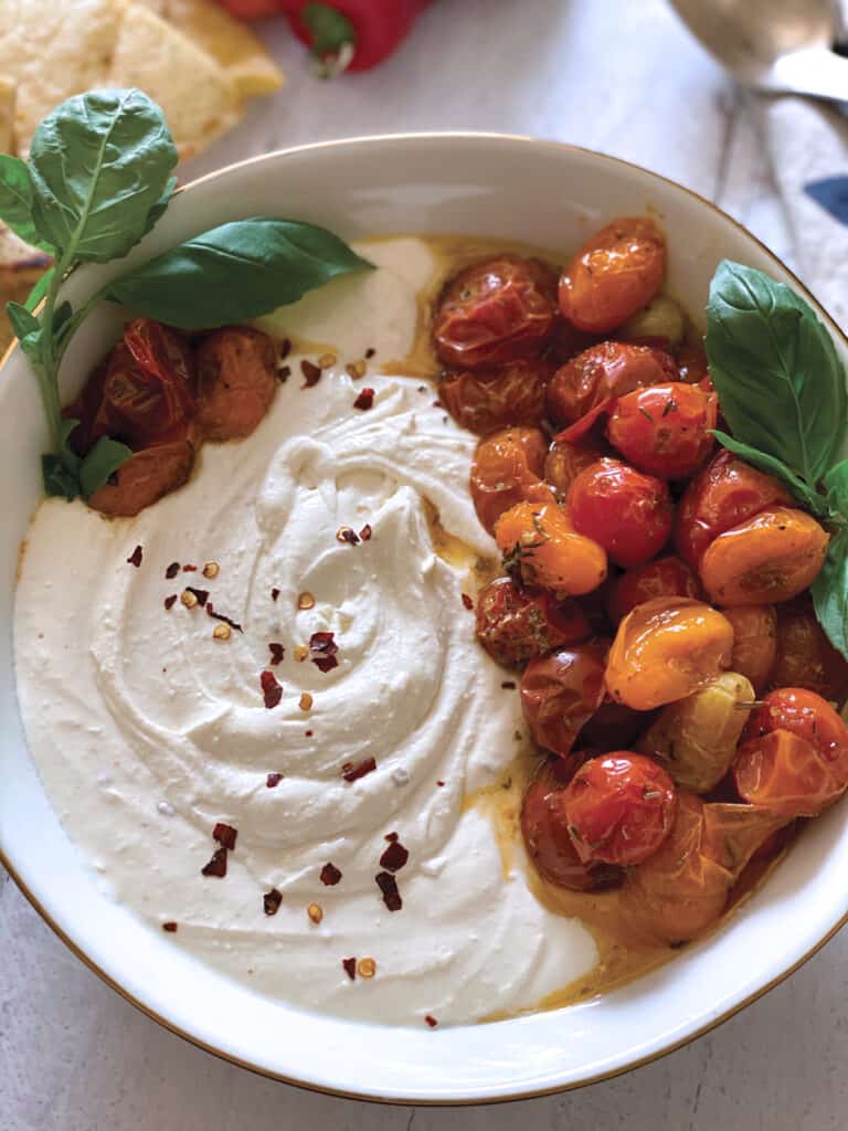 A bowl with whipped feta and roasted tomatoes. Some pita bread , peppers and a cloth napkin.