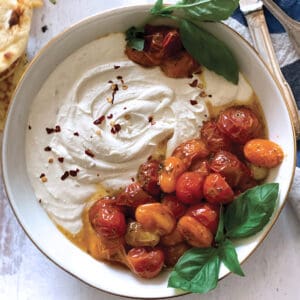 A bowl with whipped feta and roasted tomatoes. Some pita bread , peppers and a cloth napkin.