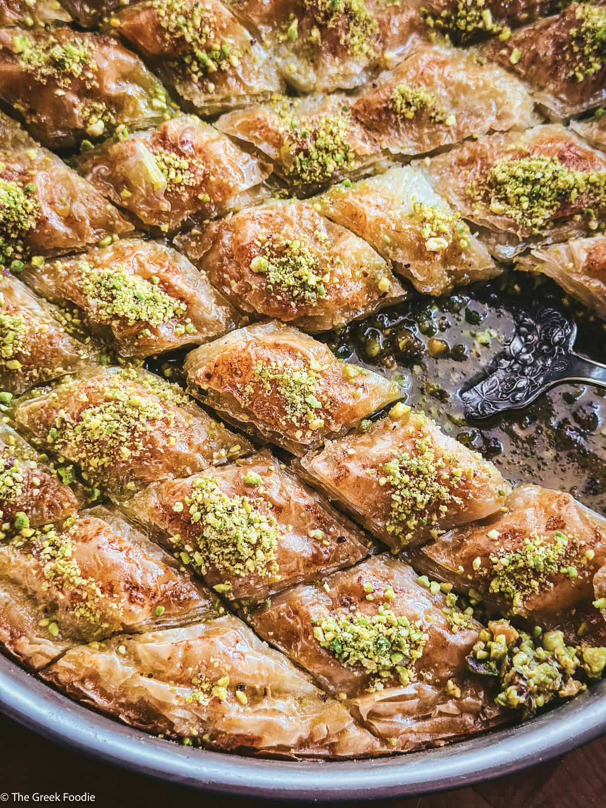 Round pan of Greek pistachio baklava cut into diamonds and topped with ground pistachios
