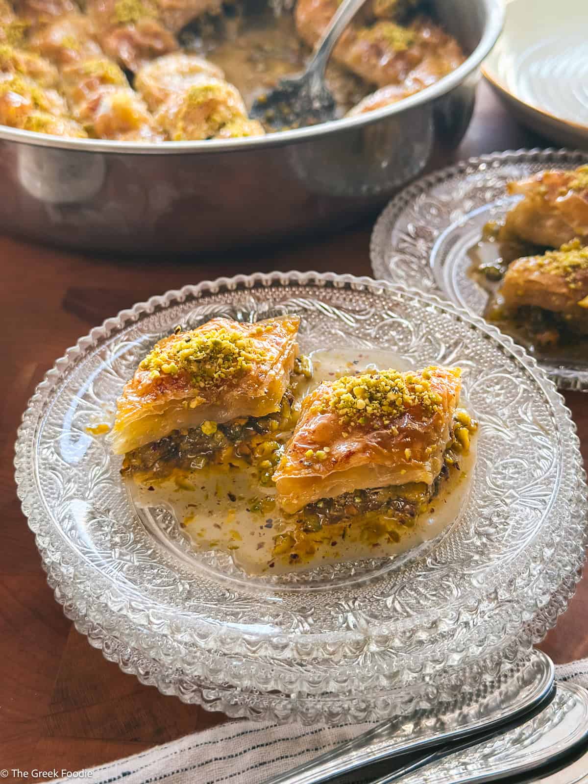 Two plates with two pieces of pistachio baklava each, with crisp phyllo layers and green pistachio filling