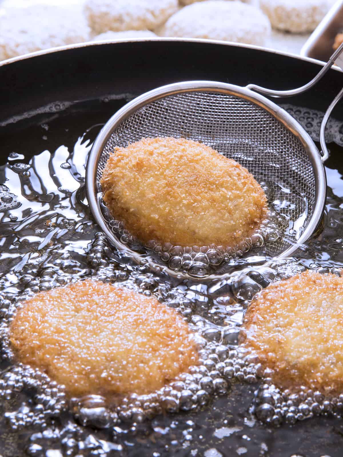 Three fish cakes frying and a spatula.