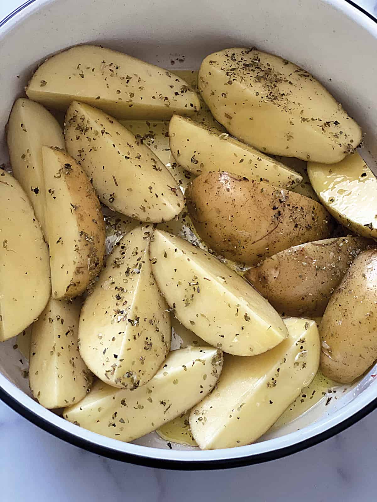 Potato wedges dressed in olive oil in a bowl.