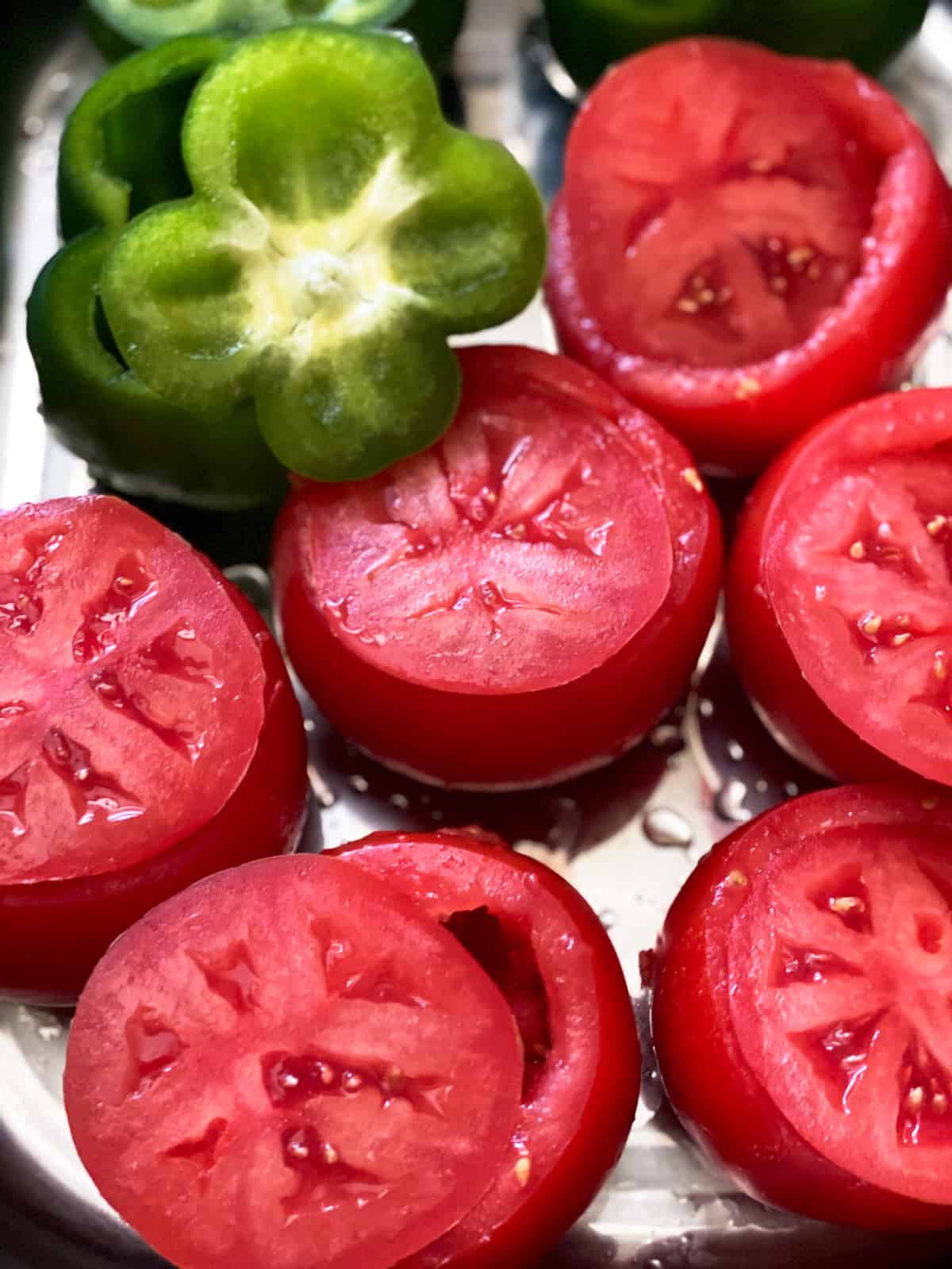 Tomatoes and green bell peppers with the tops cut, on top of each one.