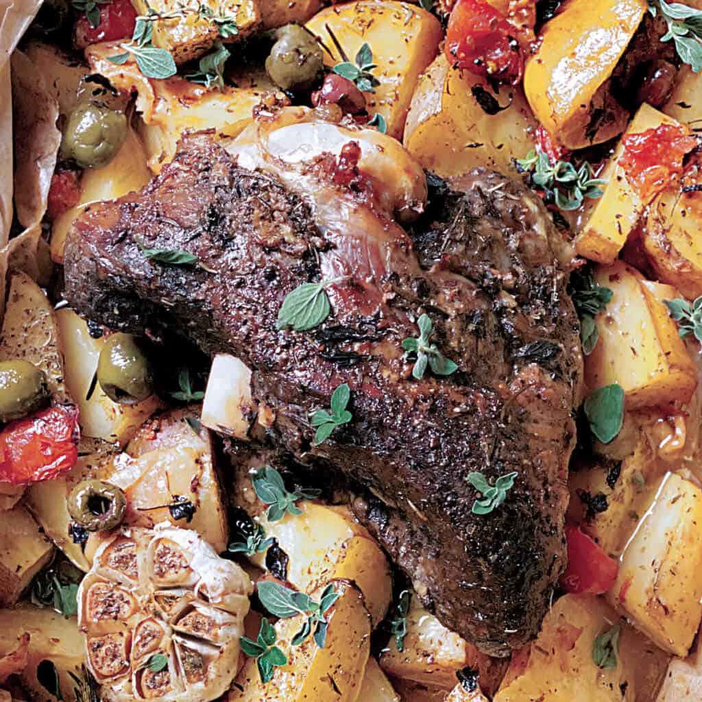 A lamb roast with potatoes, tomato, olives and garlic in parchment paper in a pan.
