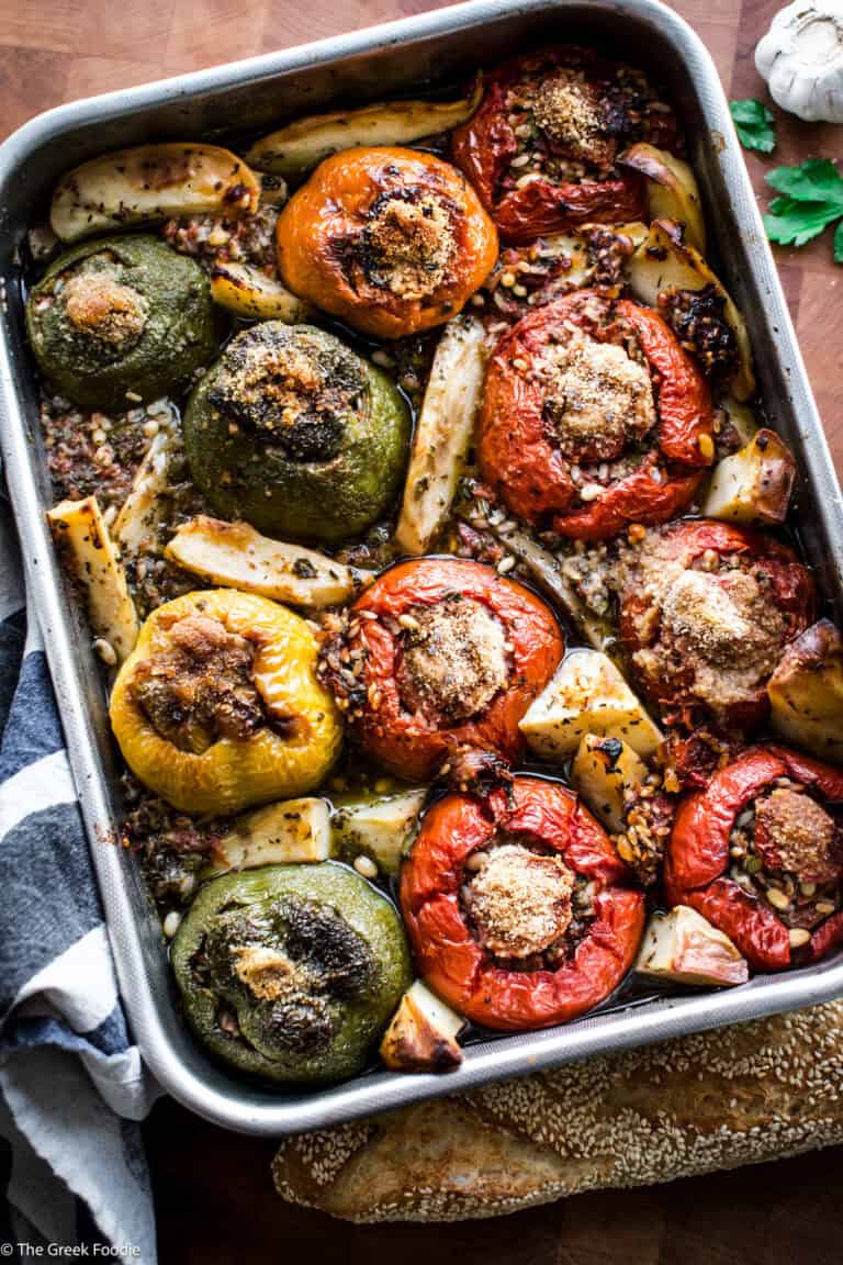 A baking pan with gemista — Greek stuffed tomatoes and bell peppers with golden potato wedges and fresh herbs