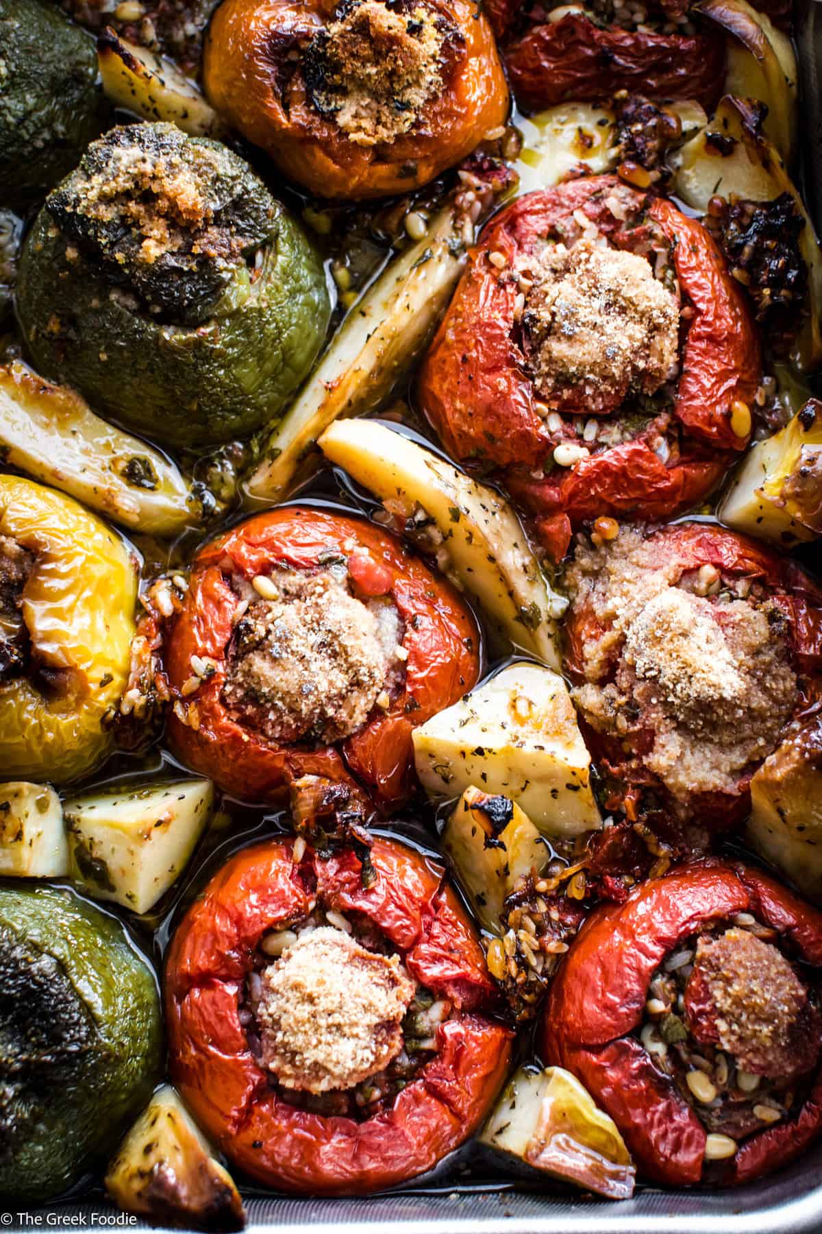 A baking pan with gemista — Greek stuffed tomatoes and bell peppers with golden potato wedges and fresh herbs