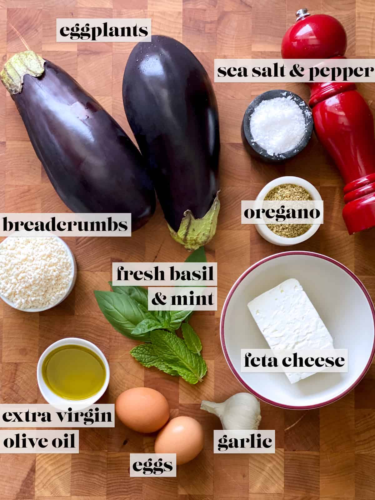Ingredients for eggplant fritters. Eggplants, small containers with salt, oregano, olive oil, breadcrumbs. some herbs, two eggs and a pepper grinder.. A bowl with feta, 