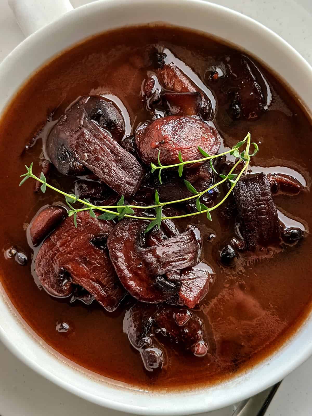 A bowl with marsala sauce with mushrooms and twigs of thyme on top.