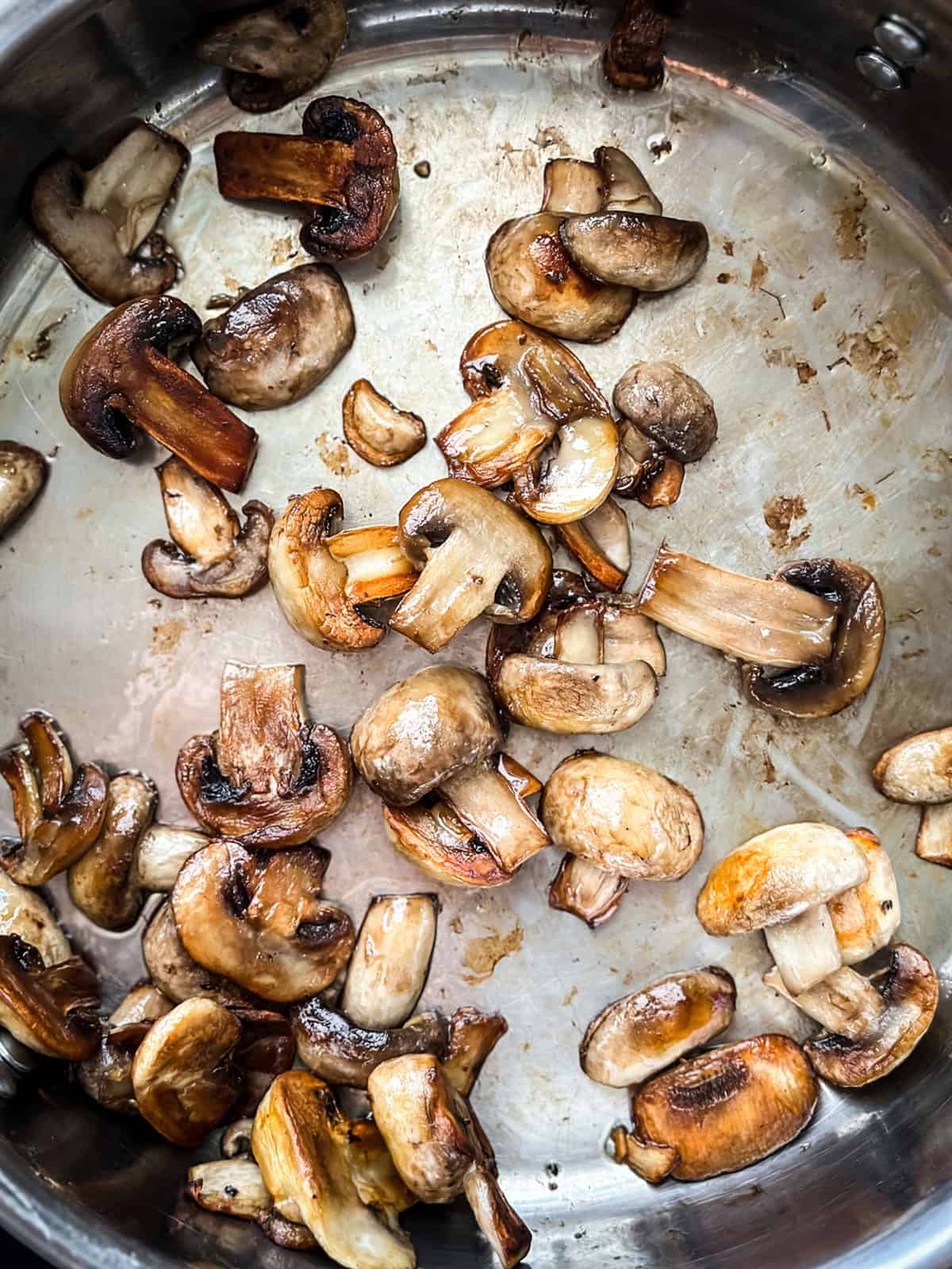 Sliced mushrooms sauteing in a skillet.