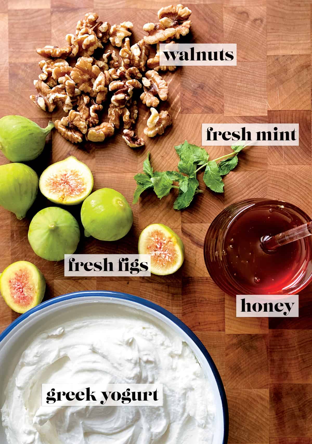 Fresh figs, walnuts, two fresh mint twigs, a pot of honey and a bowl of yogurt on a butcher block.