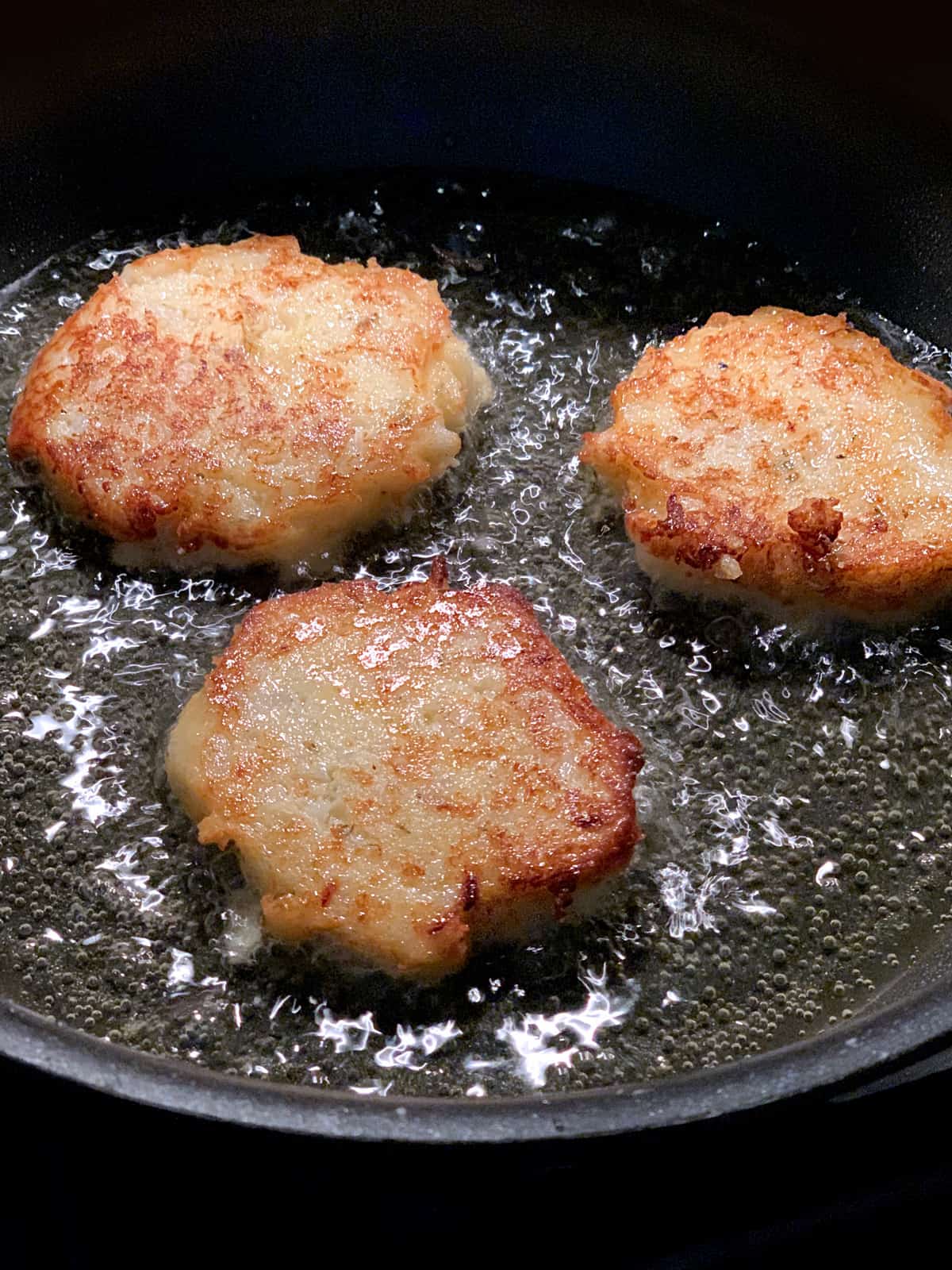 Three fritters frying in olive oil.