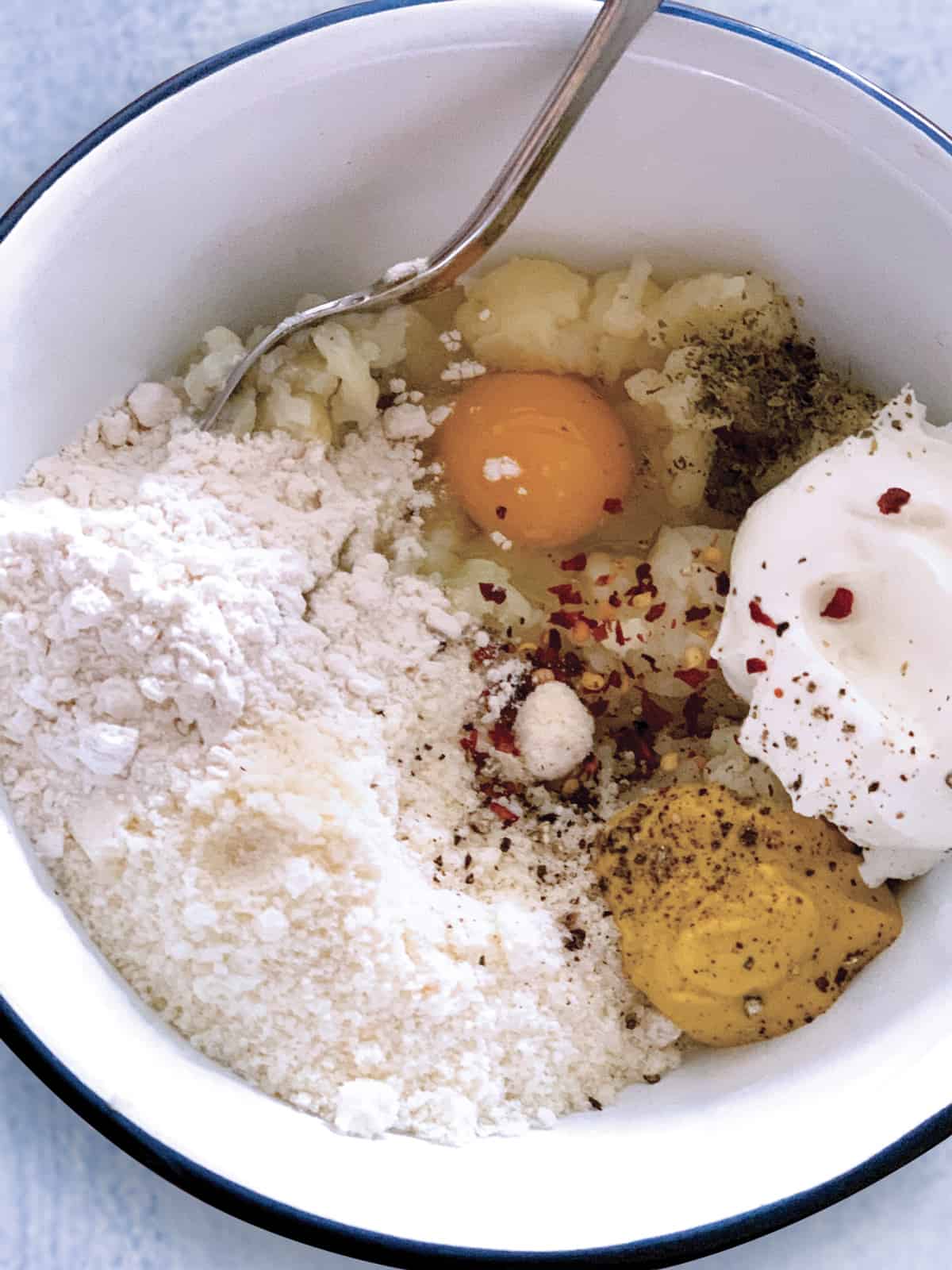 A bowl with cauliflower, flour, egg, mustard, yogurt and chili flakes.
