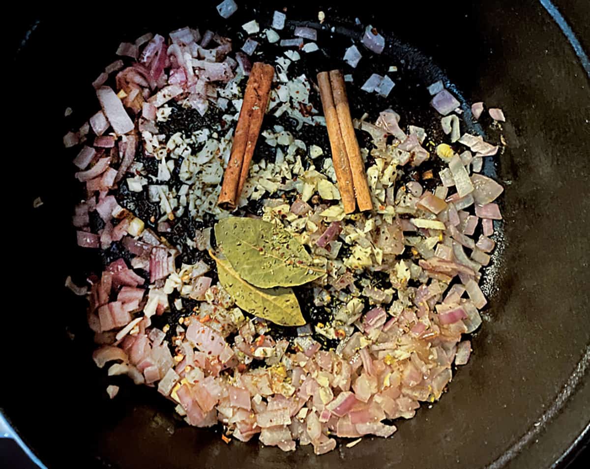 Diced onions , cinnamon sticks, bay leaves in a pot.