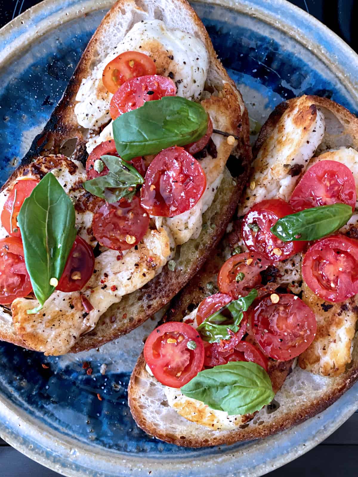 Fried halloumi and tomatoes on toast, on a plate with a cloth napkin, tomatoes and fresh herbs.