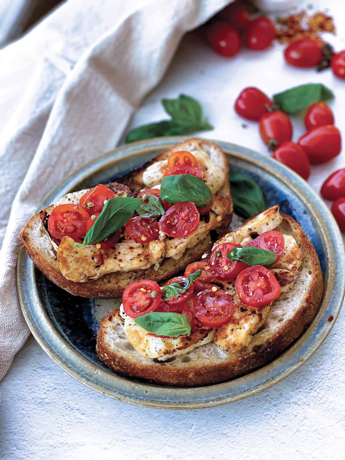 Fried halloumi and tomatoes on toast, on a plate with a cloth napkin, tomatoes and fresh herbs.
