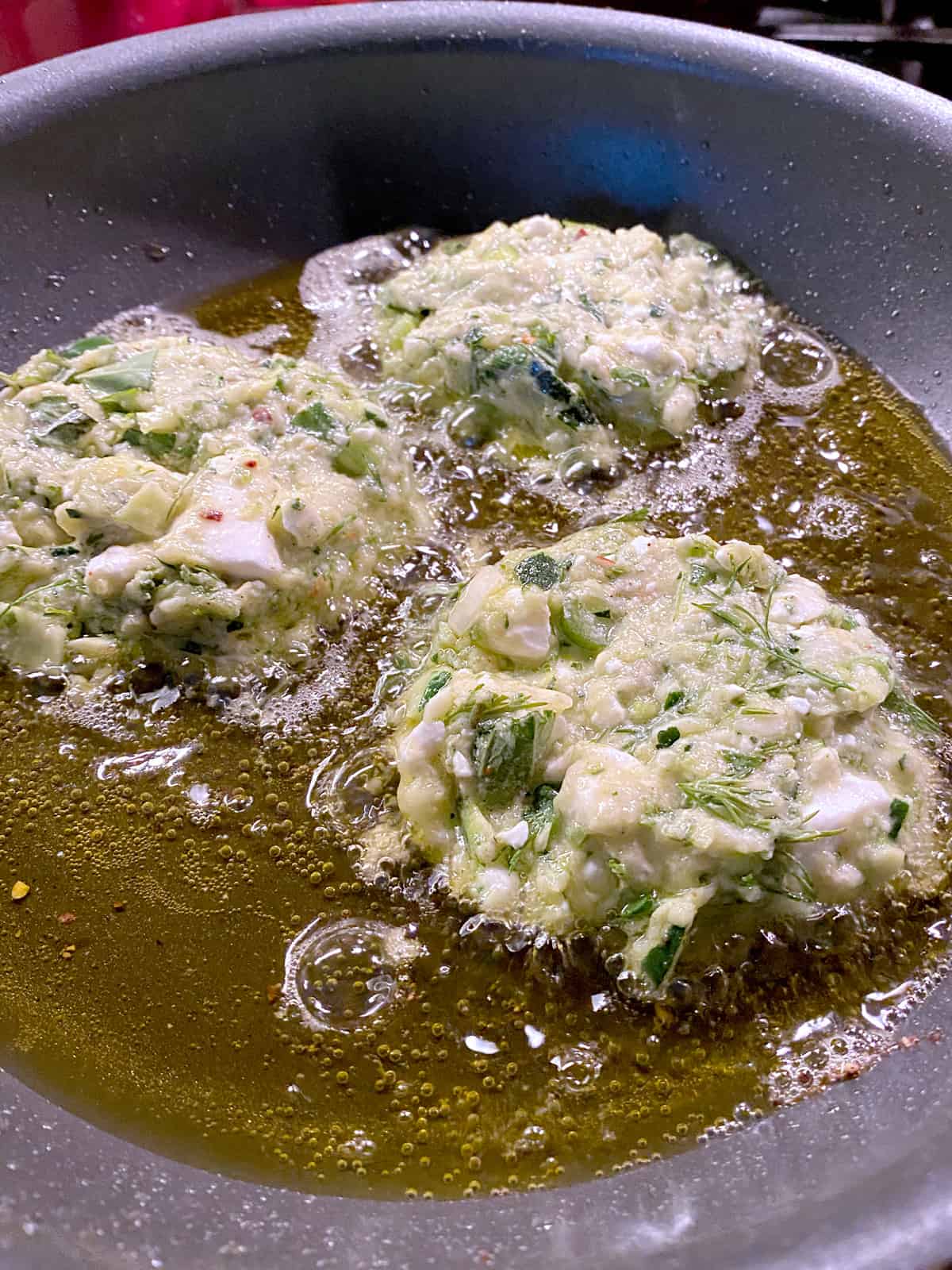 Three fritters frying in olive oil.