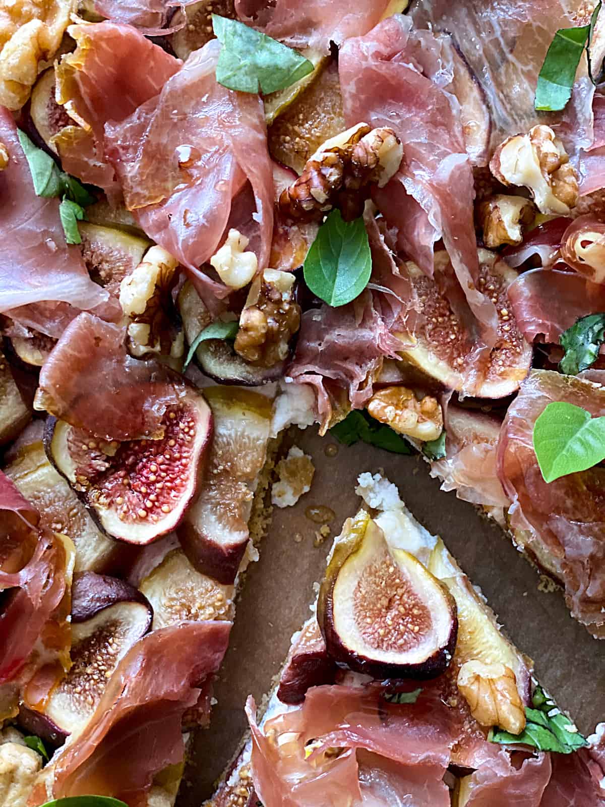 A savory galette with figs and prosciutto, a piece cut out on parchment paper.