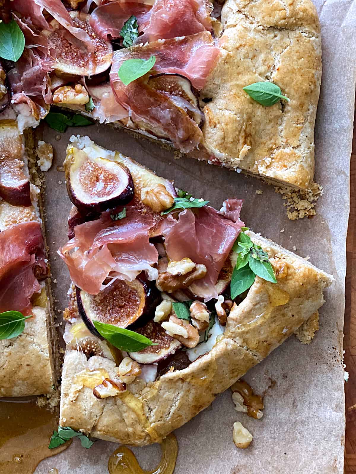 A savory galette with figs and prosciutto, a piece cut out and a honey dipper on parchment paper.