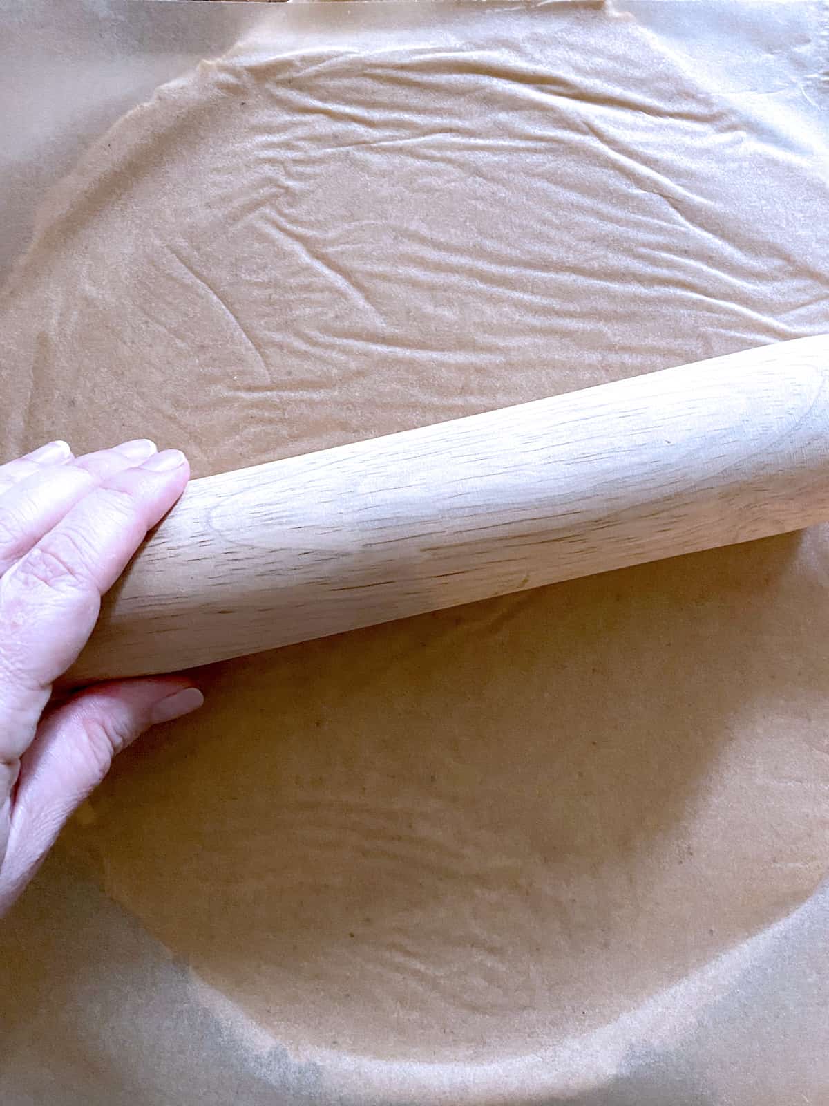 A hand on a rolling pin pn parchment paper.