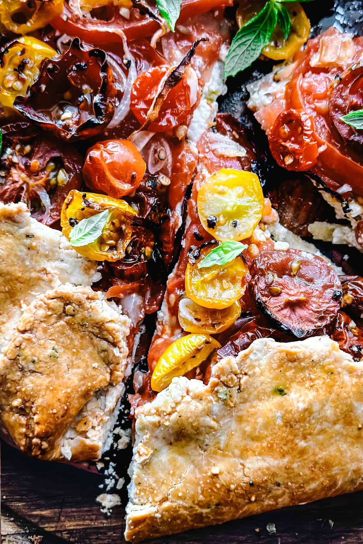 Close up of a tomato galette with feta cheese, onions and tomatoes on a cutting board with a piece cut.