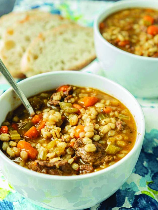 A bowl with beef and barley soup and a spoon.