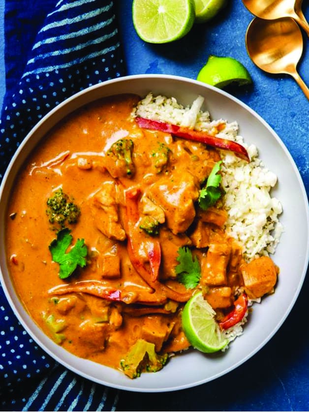 A plate with pumpkin curry with chicken and fresh veggies.