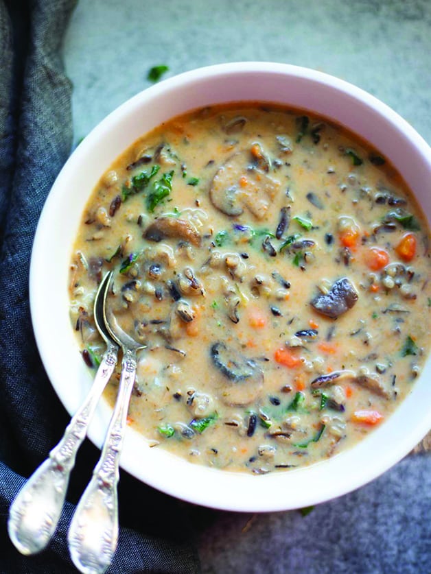 A bowl with mushroom wild rice soup and two spoons.