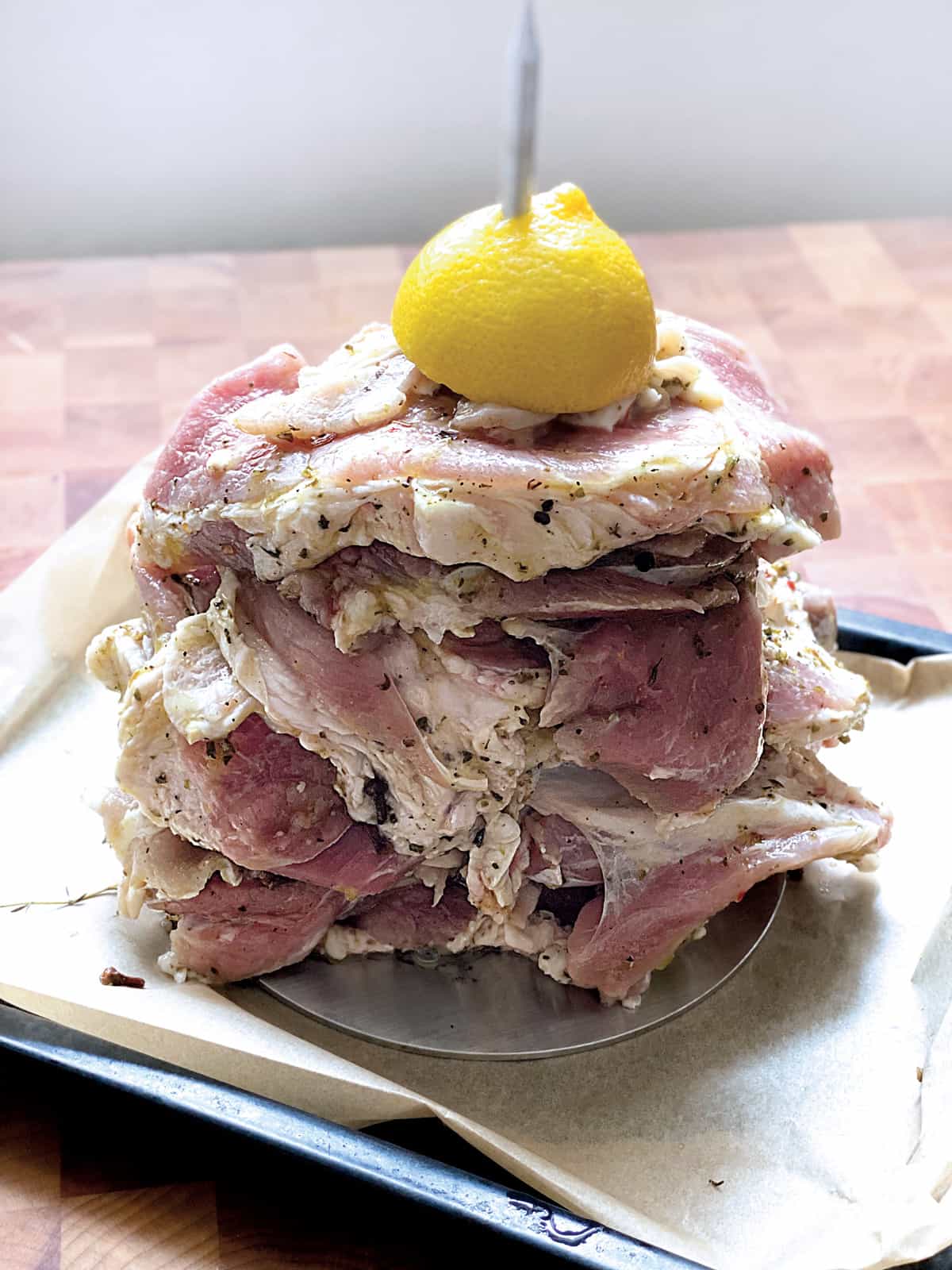 Raw pork cutlets on a vertical rotisserie with half a lemon on top, in a baking pan.