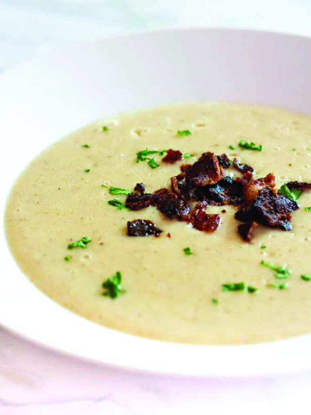 A bowl with roasted parsnip and potato soup with bacon bits on top.