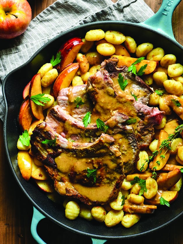 A skillet with pork chops and gnocchi.
