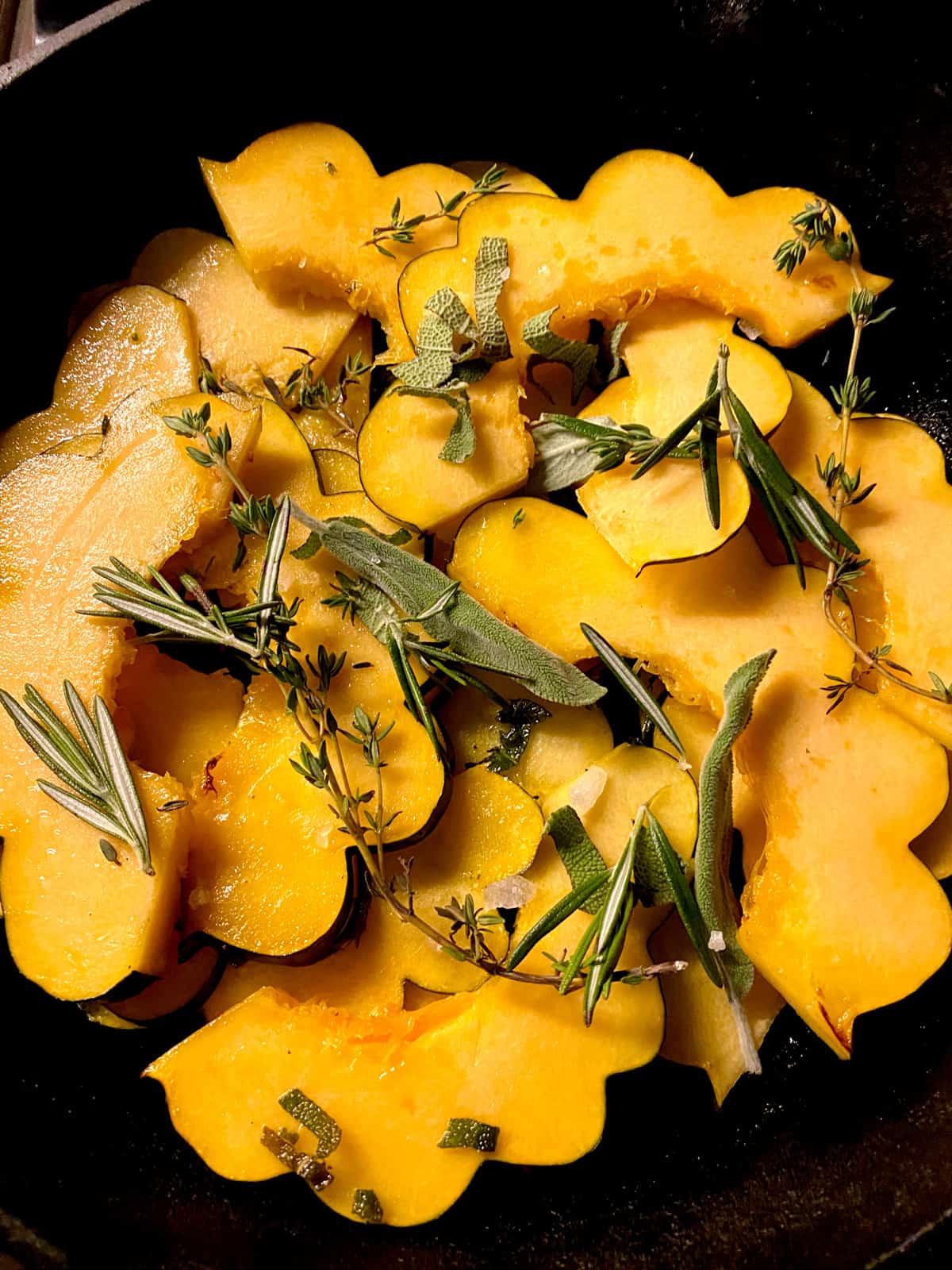 Acorn squash slices with herbs in a skillet.