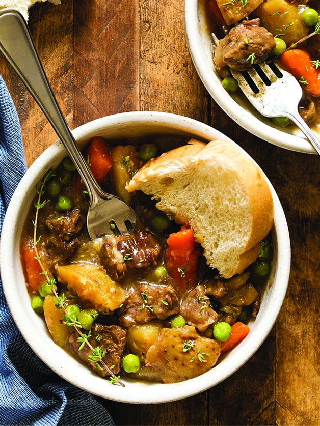 Two mini pots with beef stew with potatoes, carrots, and peas.