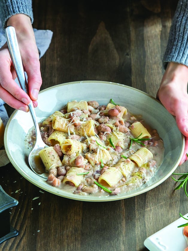 Hands holding a plate with pasta e fagioli.