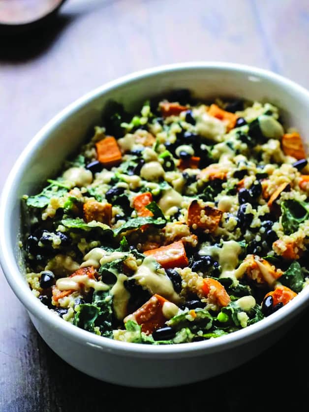 A plate with sweet potato casserole with black beans, kale, quinoa and roasted garlic sauce.