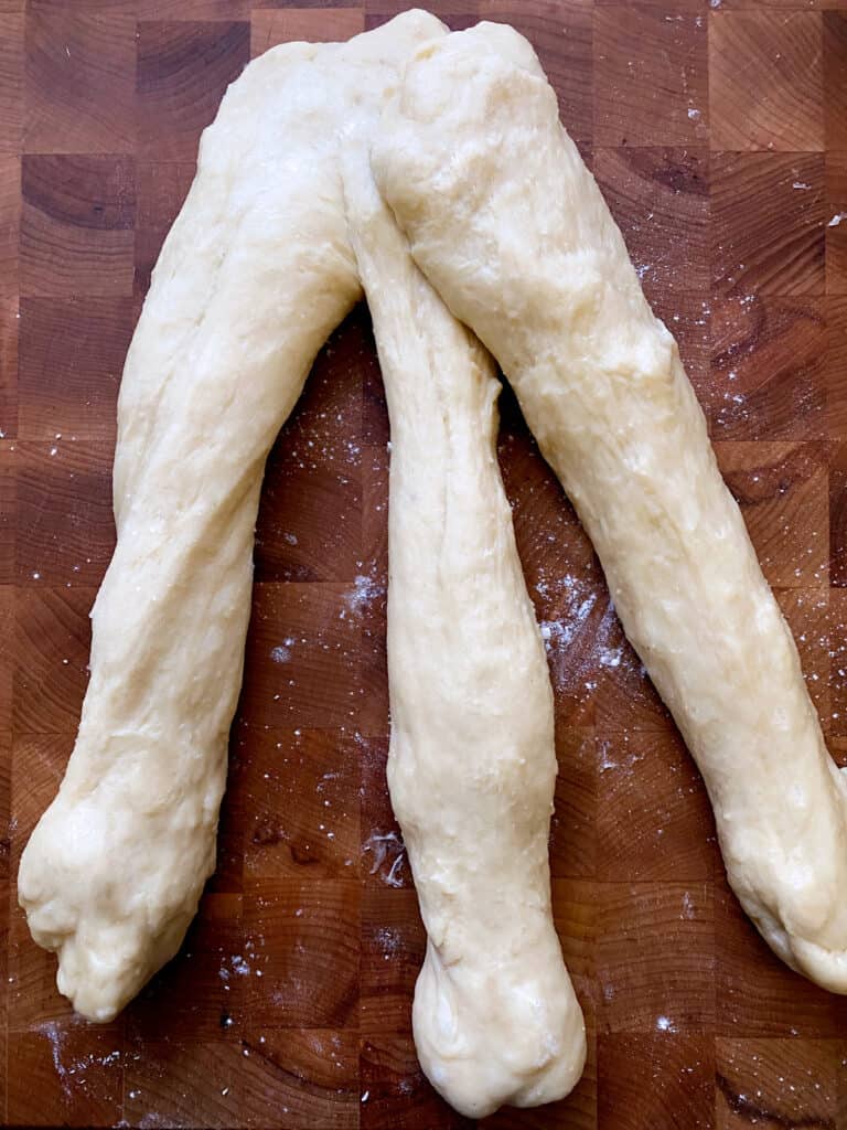 Three long pieces of dough on a butcher block.