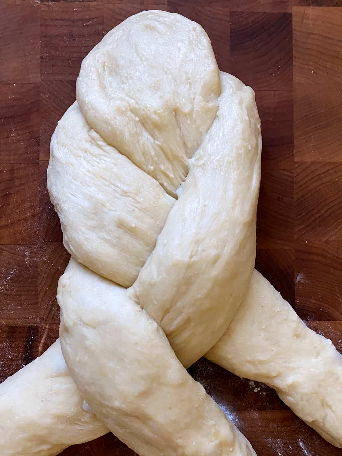 Three long pieces of dough braided on a butcher block.