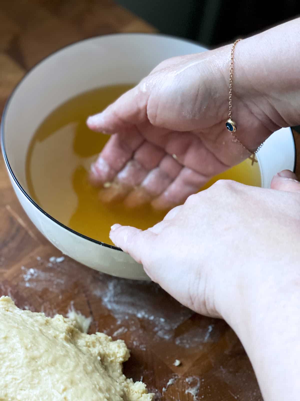 Hands bathing in anise seed tea next to a dough on a butcher block.