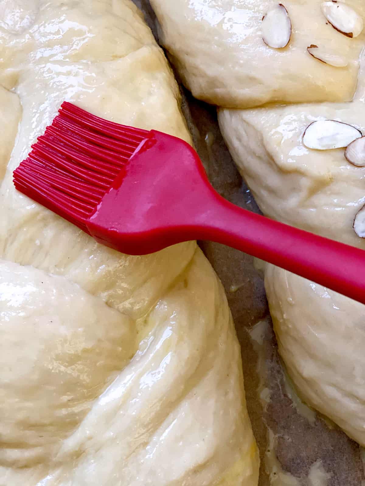 A red brush brushing egg wash on Tsoureki.