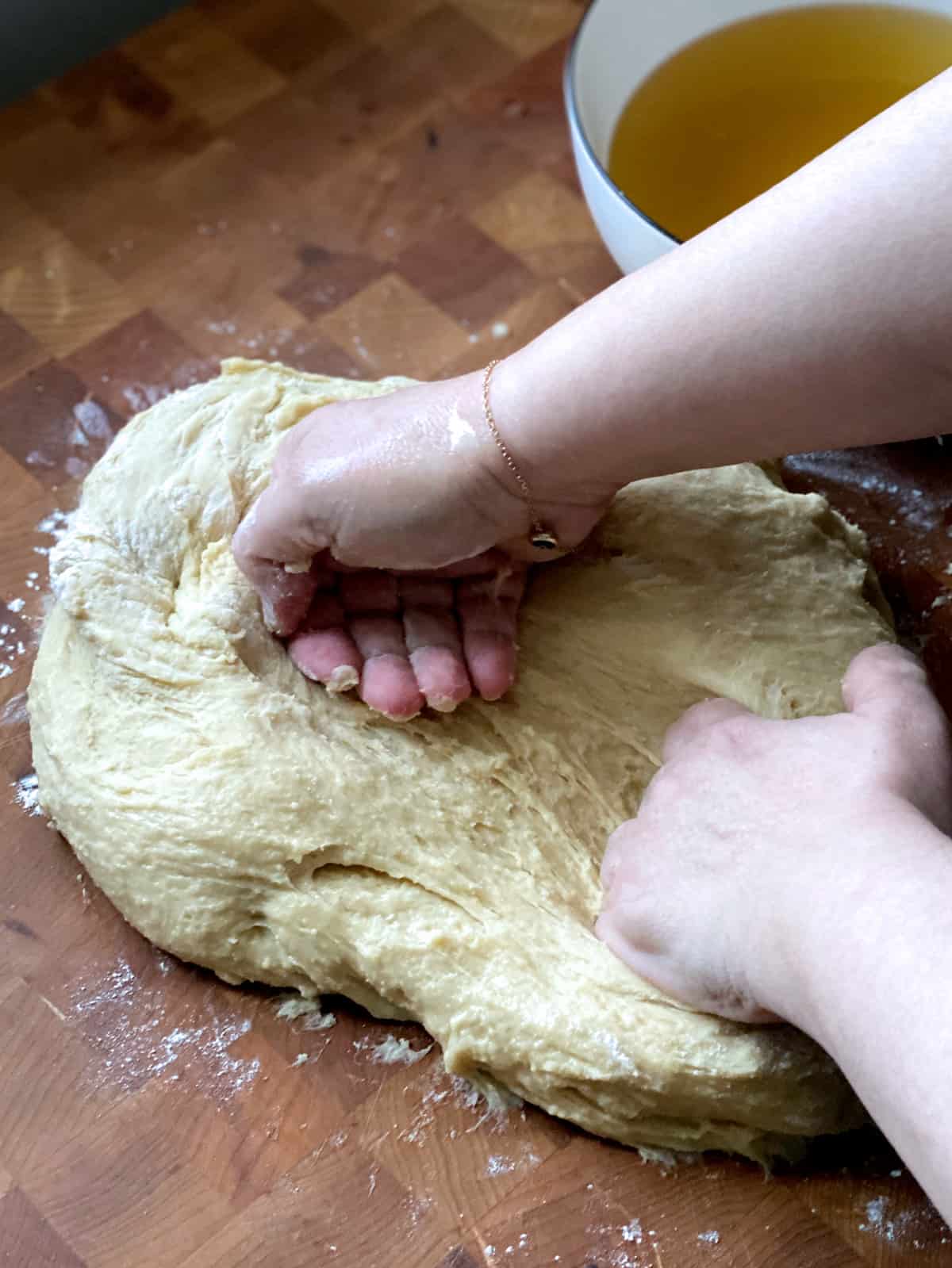 Hands kneeding dough on a butcher block.