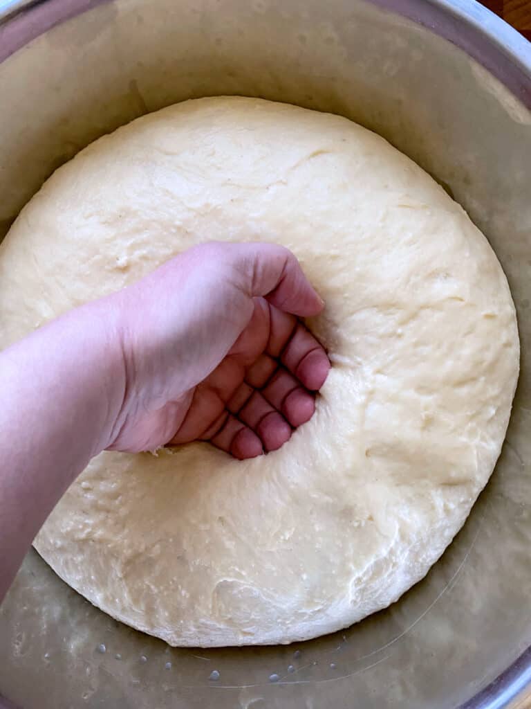 A hand punching dough in a bowl.