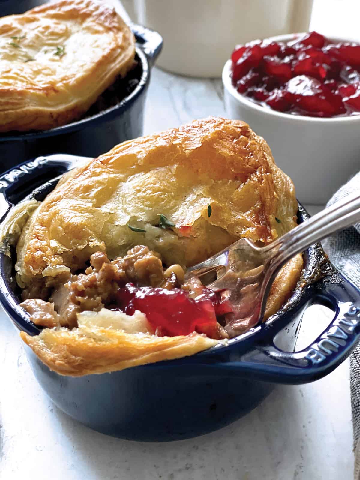 A mini pot pie with a fork inside, breaking the pastry and revealing stuffing gravy and some cranberry sauce.