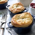 Two mini pot pies a fork and knife and a bowl with cranberry sauce at the back.