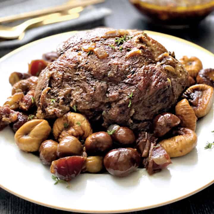 A Christmas roast on a platter surrounded with dried fruit, a gravy boat at the back in a holiday environment.
