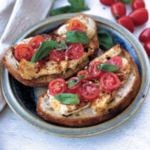 Fried halloumi and tomatoes on toast, on a plate with a cloth napkin, tomatoes and fresh herbs.