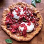 A pizza with eggplant, tomatoes and burrata cheese on a cutting board.