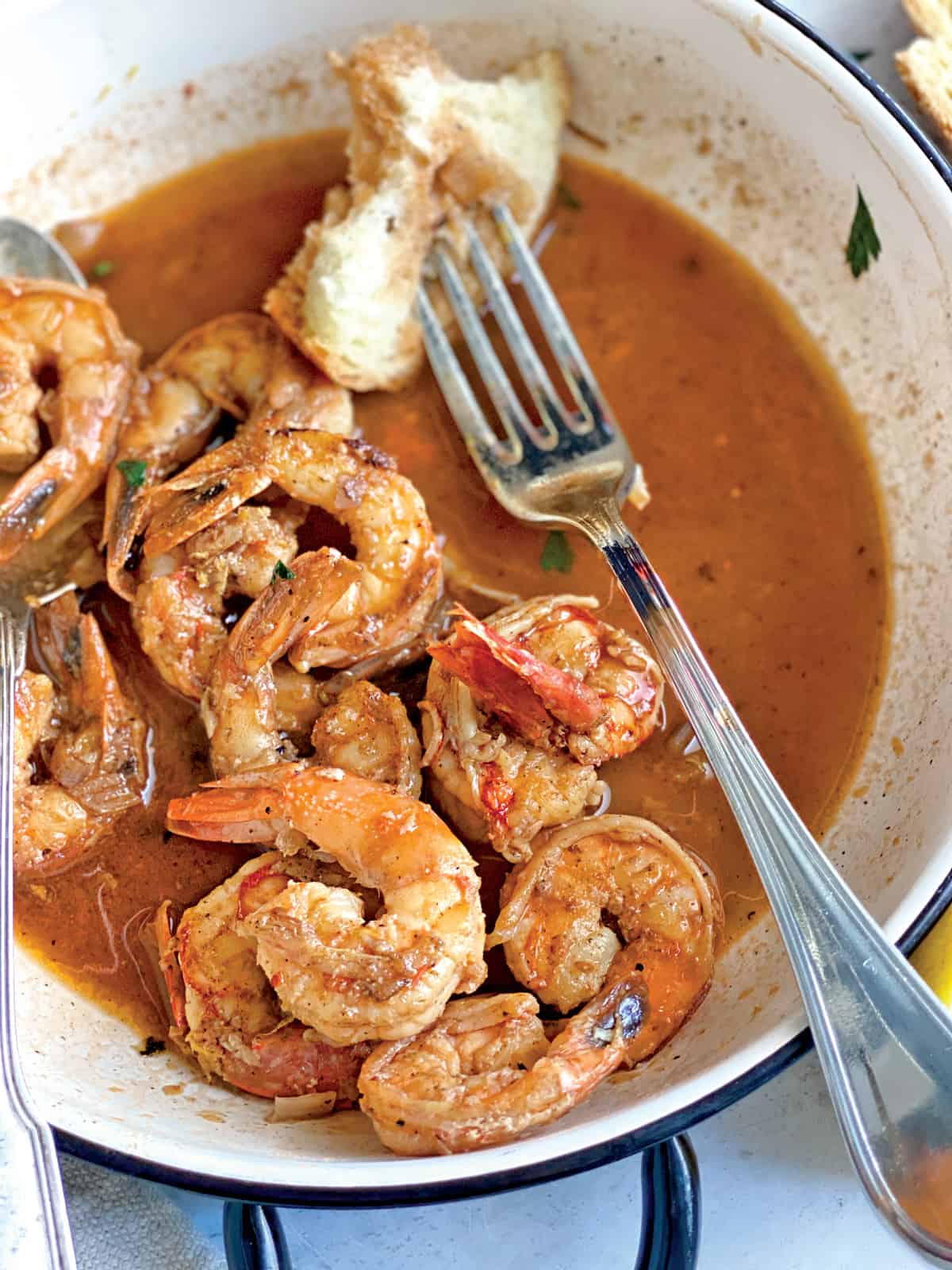 A serving dish with shrimp in a lemon garlic wine sauce and a fork with a piece of bread.