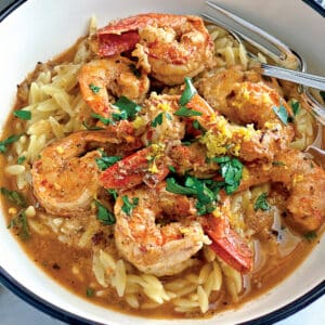 A bowl with shrimp orzo in lemon butter sauce and utensils.